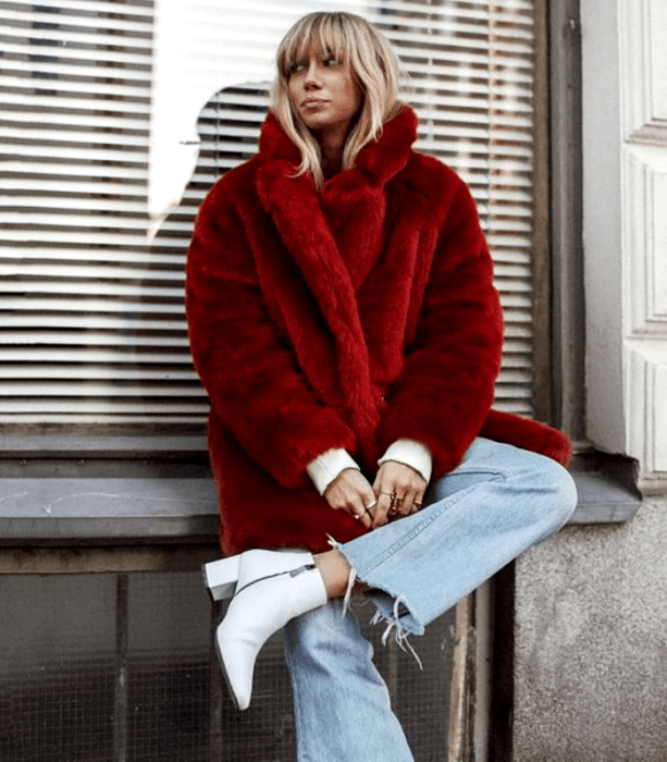 chica rubia usando un abrigo rojo afelpado, jeans holgados rectos, botines blancos de tacón y top blanco de manga larga