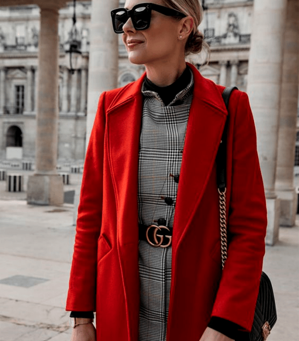 chica rubia usando lentes de sol, abrigo largo rojo, vestido gris de cuadros, cinturón negro gucci y bolso de mano negro