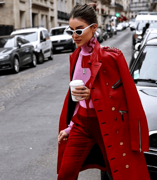 chica de cabello oscuro usando lentes de sol blancos, suéter rosa de cuello alto con estampado rojo, abrigo largo rojo, pantalones rojos de vestir 