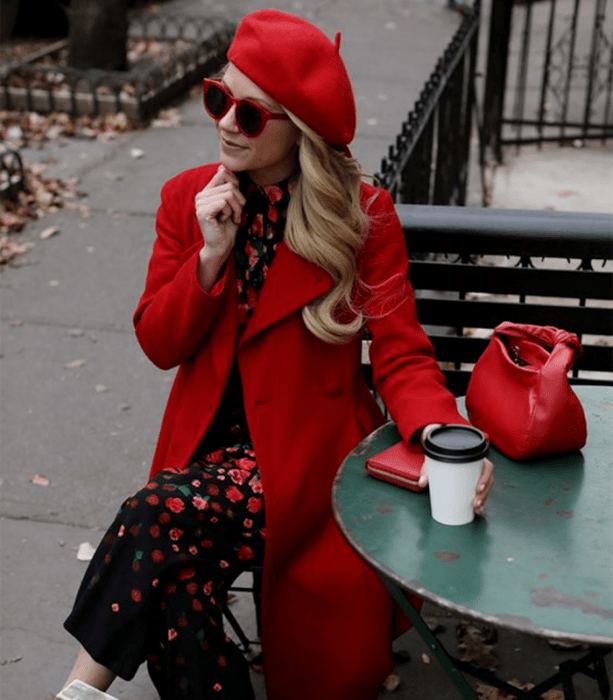 chica rubia usando lentes de sol rojos, beret rojo, vestido negro con flores rojas, abrigo rojo largo y bolso de mano rojo