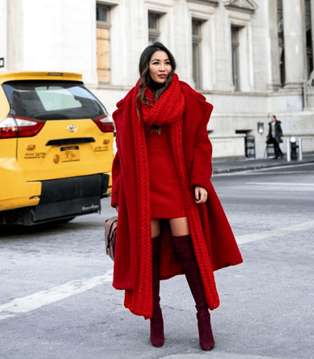 chica de cabello castaño usando una bufanda roja larga, vestido mini rojo, botas largas guindas de terciopelo, abrigo largo rojo y bolso de mano café