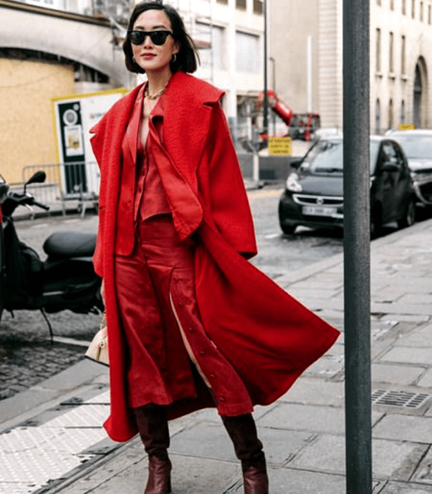 chica de cabello corto usando lentes negros de sol, abrigo largo rojo, top rojo de satén con cuello en V, falda de satén roja con botones al frente y botas largas guindas