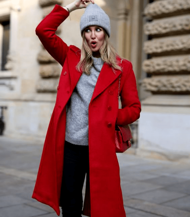 chica rubia usando un gorro beanie gris, suéter gris, abrigo largo rojo, jeans negros holgados y bolso de mano rojo