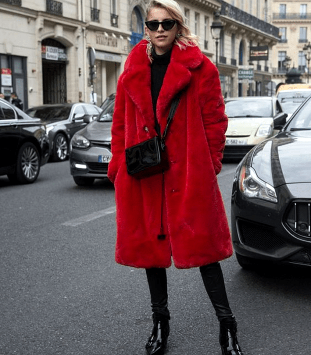 chica rubia usando lentes de sol, abrigo largo afelpado rojo, top negro de cuello alto, bolso de mano negro, skinny jeans negros, botines negros de charol con tacón