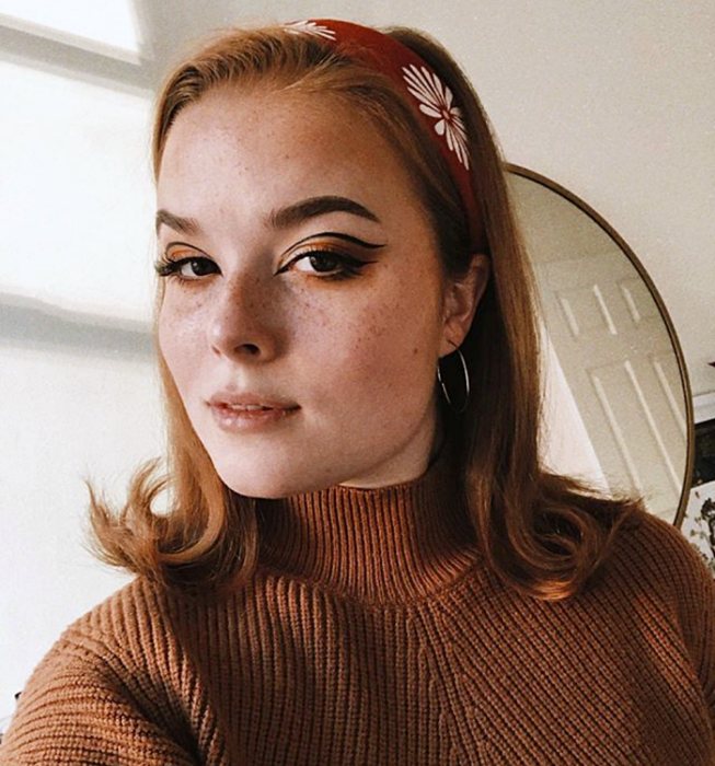 chica pelirroja usando maquillaje estilo retro, vintage de los años 60 y 70 con delineado gráfico negro y sombras naranjas, cafés y beige