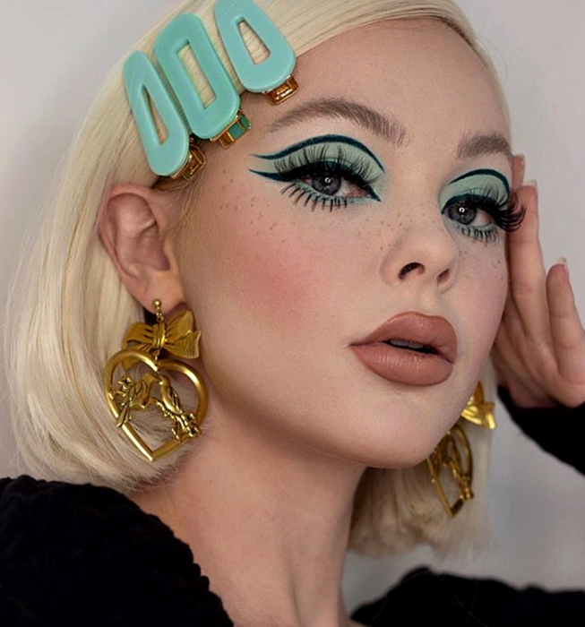 blondes Mädchen, das ein Retro-Make-up im Vintage-Stil aus den 60er und 70er Jahren mit hellblauem Lidschatten und dickem schwarzen grafischen Umriss mit falschen Wimpern trägt
