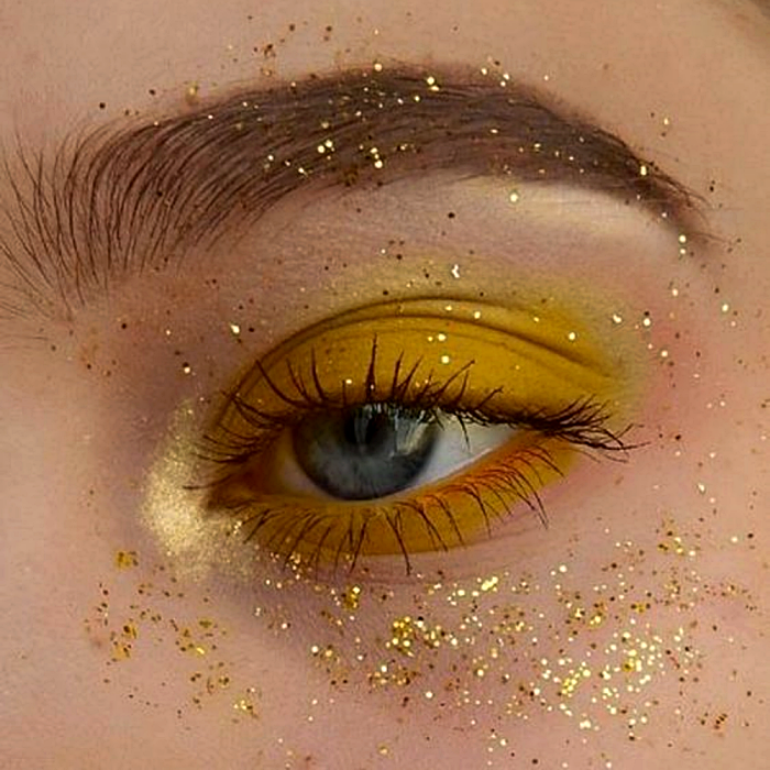 maquillaje con sombras amarillas, delineado naranja, dorado y glitter amarillo y naranja