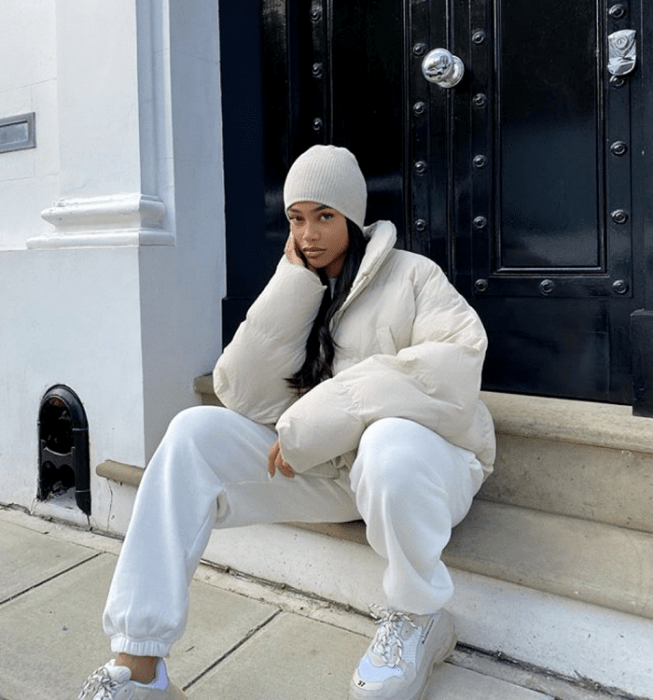 chica morena usando un gorro beine beige, chamarra puff jacket beige, pants blancos, tenis deportivos blancos