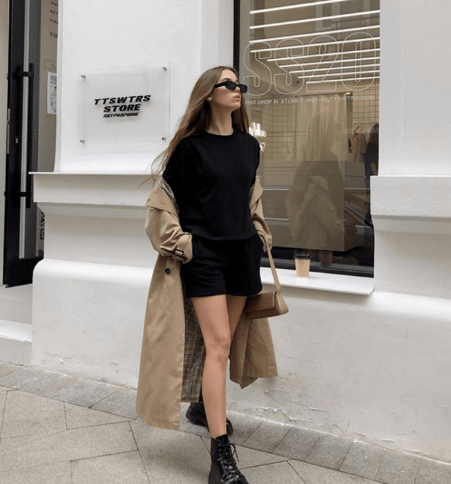 chica rubia usando lentes de sol, camiseta negra, shorts negros, abrigo beige, botas de suela gruesa y bolso mini de piel beige