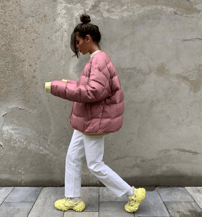 chica de cabello castaño usando una chamarra rosa puffer jacket, jeans blancos, tenis amarillos neón y sudadera blanca