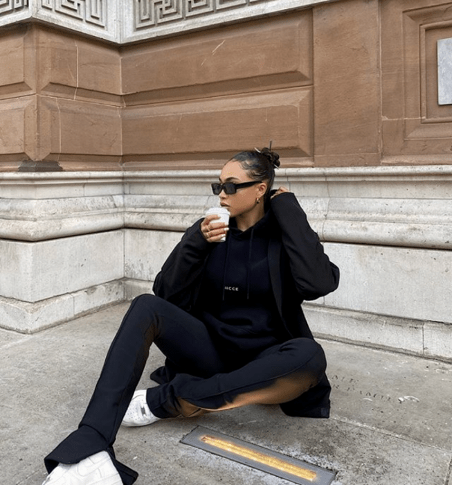 chica morena usando lentes de sol, sudadera negra, leggings negros, abrigo negro, tenis blancos