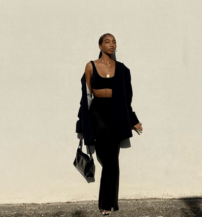 chica morena usando un crop top negro, blazer negro oversized, pantalones de vestir negros, sandalias negras de tacón y bolso de mano negro