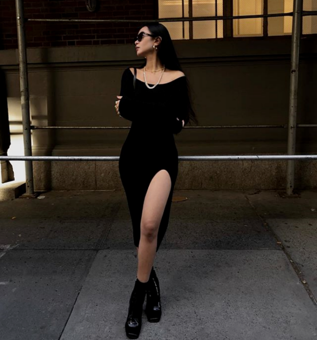 chica de cabello castaño usando lentes de sol, vestido tejido negro con escote abierto, abertura en la pierna, botas de cuero negras con plataforma y suela gruesa
