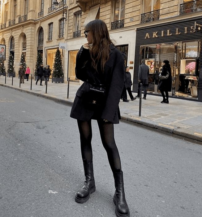 chica de cabello castaño usando lentes de sol, blazer negro oversized, medias negras, botines negros de plataforma, bolso de mano negro mini de cuero