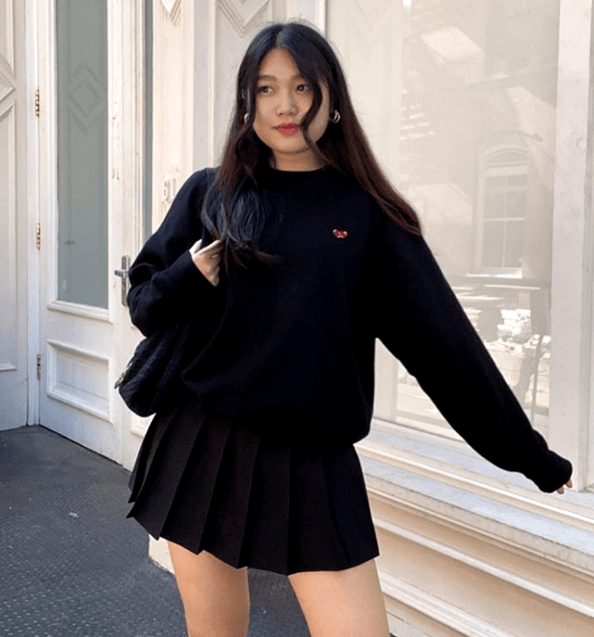 chica de cabello largo usando una sudadera negra, minifalda negra de tablones y bolso de mano negro