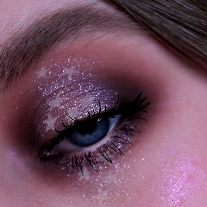 maquillaje de ojos con sombras metálicas, moradas y guindas, glitter rosa y formas de estrellas