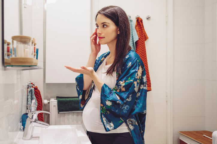 Mujer embaraazada aplicándose cremas frente al espejo