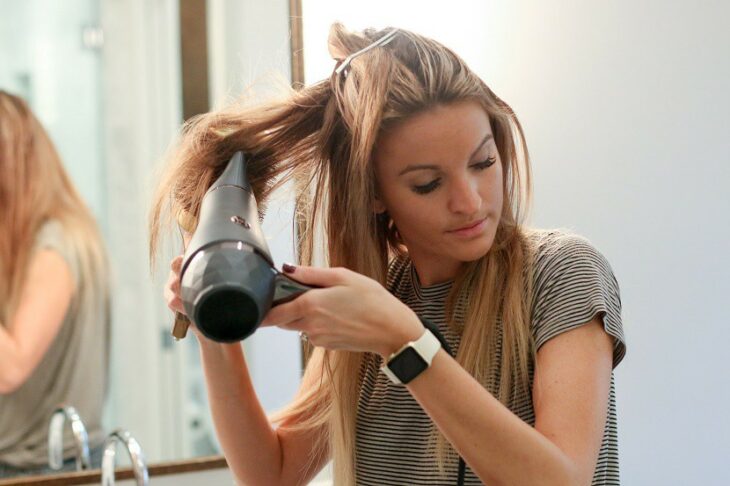 Chica secando su cabello con una secadora y un cepillo grueso