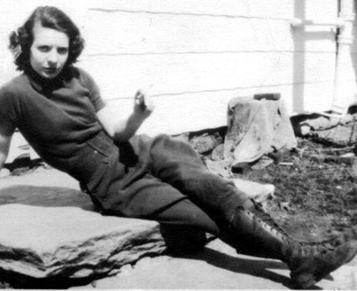 Foto vintage, fotografía antigua en blanco y negro de mujer sentada en el suelo, con cabello corto, jeans holgados y botas de trabajo