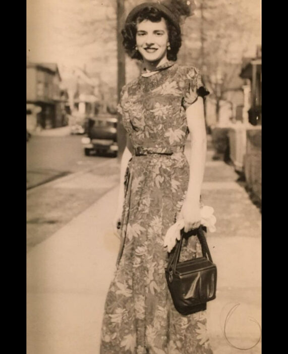 Foto vintage, fotografía antigua color sepia de mujer en la calle, con cabello corto y chino, sombrero, vestido largo de flores y bolsa negra