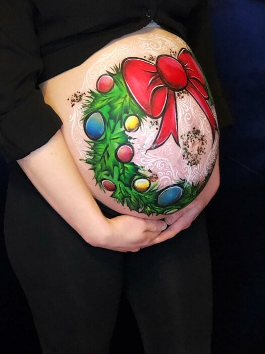 Mujer con la pancita pintada con corona navideña; Ideas para pintar tu panza de embarazada este diciembre