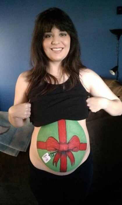Chica pintada con una regalo navideño en la pancita; Ideas para pintar tu panza de embarazada este diciembre