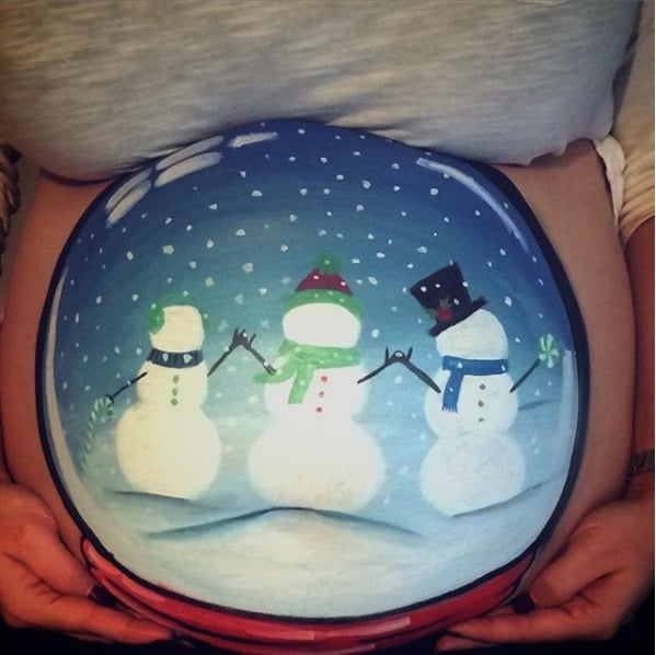 Chica con la pancita pintada en esfera de nieve con mulecos de nieve; Ideas para pintar tu panza de embarazada este diciembre