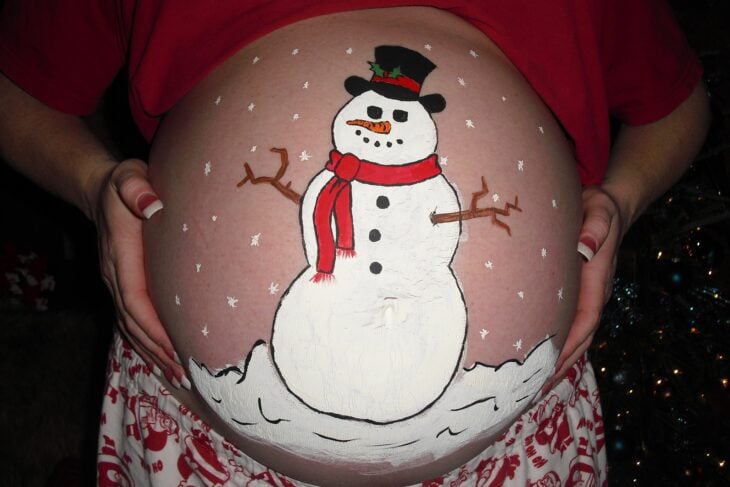 Mujer con la pancita pintada con un mono de nieve; Ideas para pintar tu panza de embarazada este diciembre