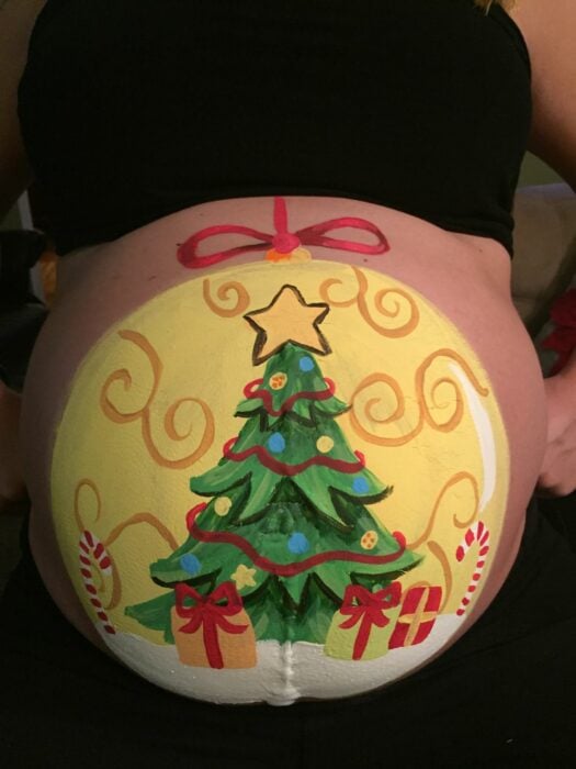 Mujer con la pancita pintada de esfera navideña; Ideas para pintar tu panza de embarazada este diciembre