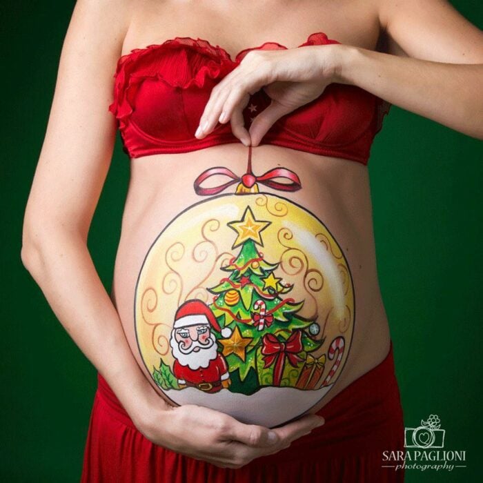 Chica con la pancita pintada con esfera navideña; Ideas para pintar tu panza de embarazada este diciembre
