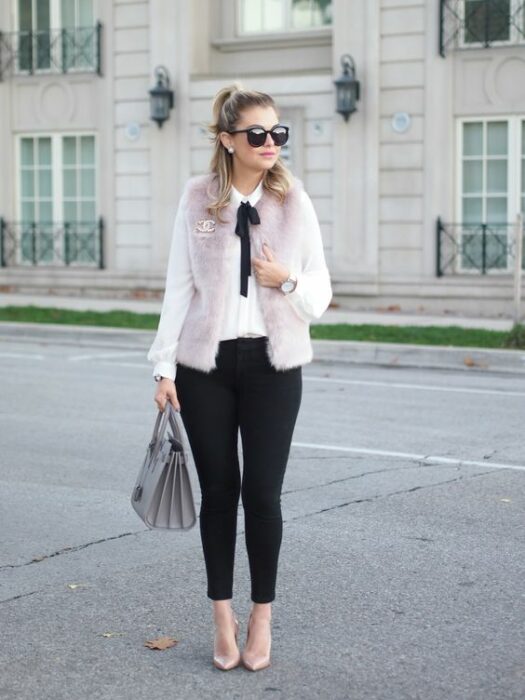 Chica rubia con media coleta y lentes de sol vistiendo pantalón negro, camisa blanca, abrigo rosa de peluche con un moño negro en el cuello