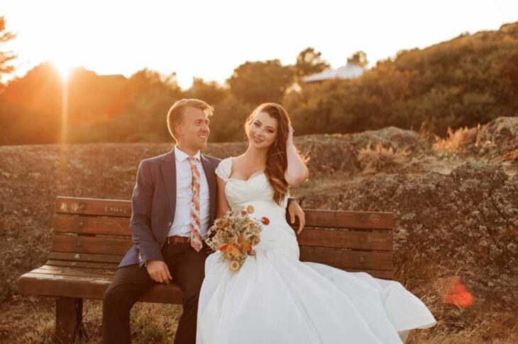 Lauren y Brayden Faganello en día de su boda sentados en una banca de madera en el atardecer 