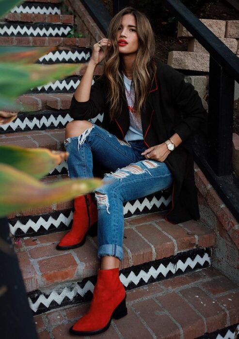 Chuica usando blazer negro, playera blanca, jeans rasgados y botines color rojo