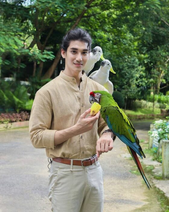 Paing Takhon posando con una guacamaya en el brazo izquierdo vistiendo camisa beige y pantalón blanco