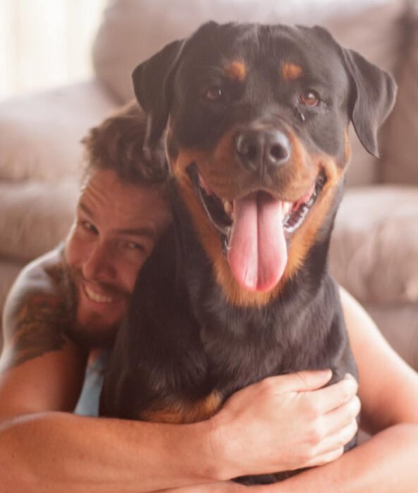 Perros sonriendo; perrito adulto rottweiler con su dueño abrazándolo