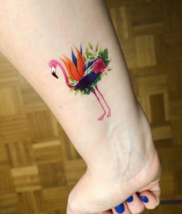 Tatuaje bonito y femenino de ave en la muñeca, pájaro flamenco con flores