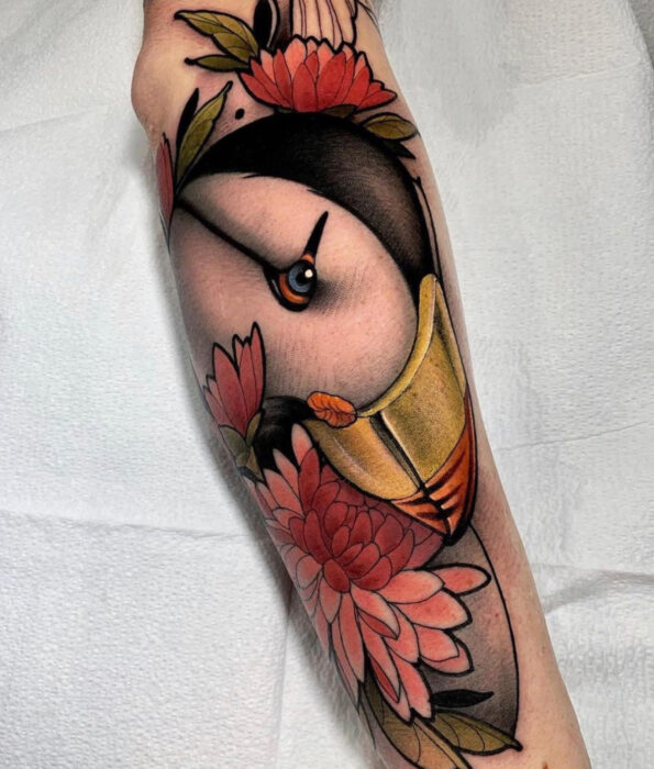 Tatuaje bonito y femenino de ave en el brazo, pájaro frailecillo realista con flores