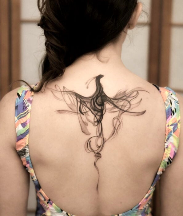 Tatuaje bonito y femenino de pájaro en la espalda, ave fénix hecha de humo