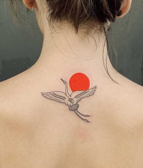 Tatuaje bonito y femenino de ave en la espalda, pájaro grulla volando sobre un sol rojo