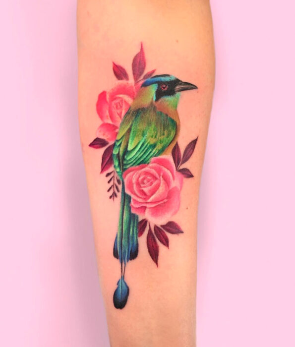 Tatuaje bonito y femenino de ave en el brazo, pájaro barranquero verde con flores rosas