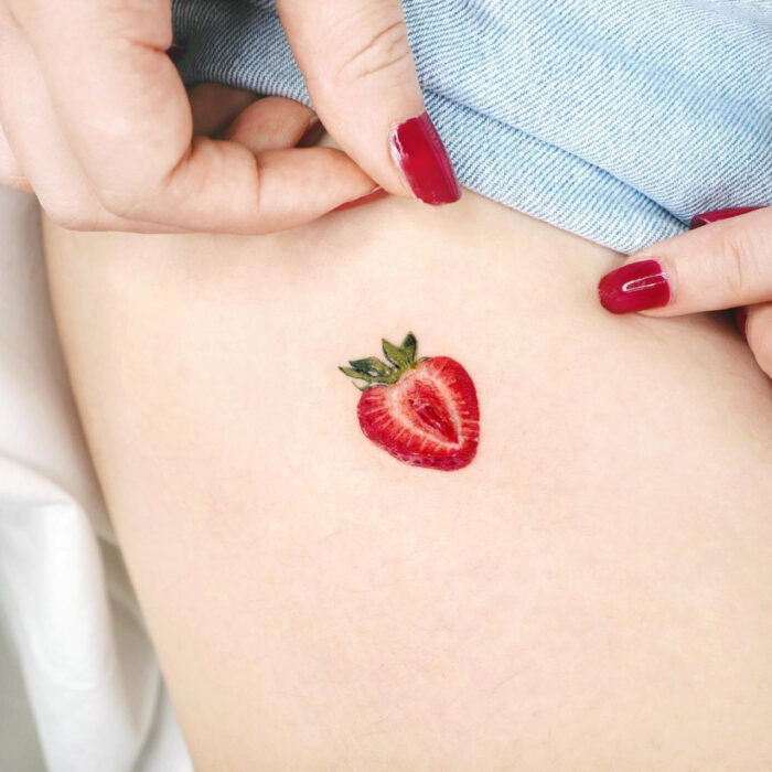 Tatuajes bonitos, pequeños y femeninos; tatuaje minimalista de fresa partida a la mitad en la pierna