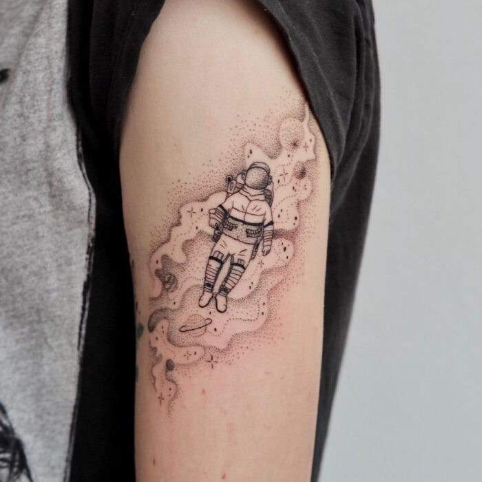 Tatuajes bonitos, pequeños y femeninos; tatuaje de astronauta en el espacio con técnica de puntillismo en el brazo