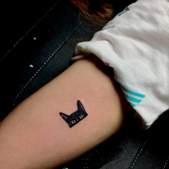 Tatuajes bonitos, pequeños y femeninos; tatuaje de gato negro con ojos amarillos en el brazo