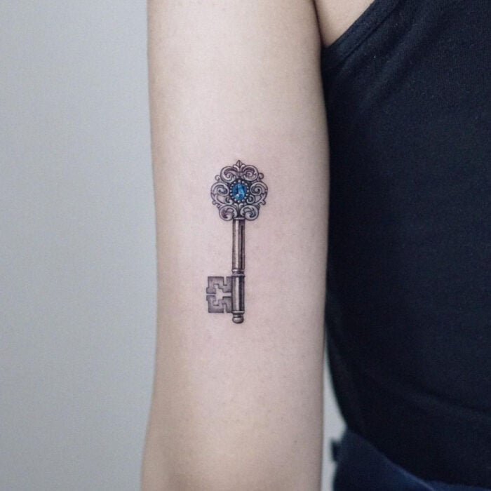 Tatuajes bonitos, pequeños y femeninos; tatuaje de llave antigua con piedra azul en el brazo