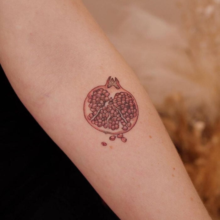 Tatuajes bonitos, pequeños y femeninos; tatuaje de granada partida a la mitad en el brazo