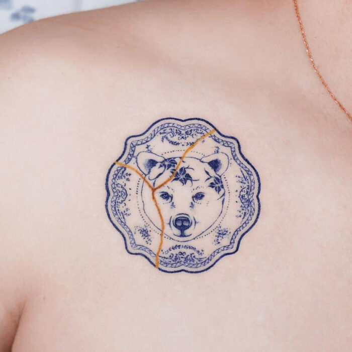 Tatuajes bonitos, pequeños y femeninos; tatuaje estilo japonés, de vajilla azul con cara de oso, kintsugi en las clavículas