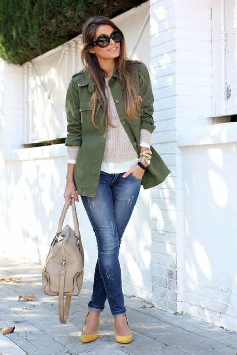 Chica usando tacones, jeans y blusa blanca a juego de un blazer color verde army y un bolso de mano color beige