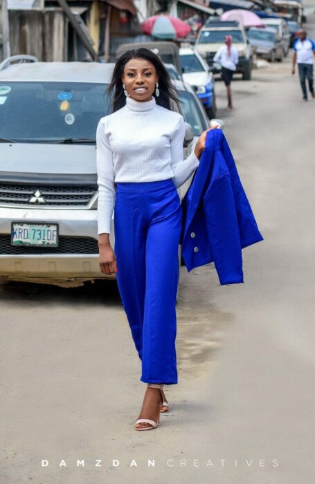 Chica llevando traje azul rey, caminando por la calle y clebrando su graduación; Vivía en edificios sin terminar, no tenía recursos, pero logró graduarse con honores 