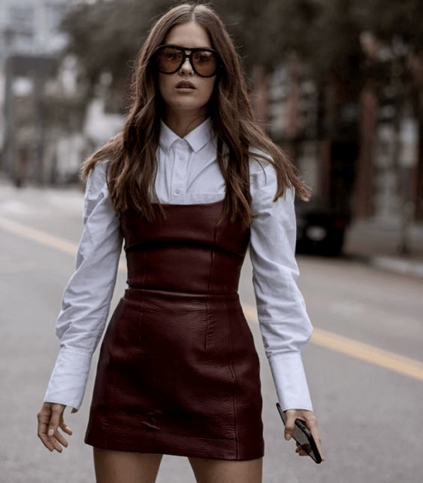 chica de cabello claro usando lentes de sol, vestido guinda rojo de cuero ajustado, camisa blanca de manga larga