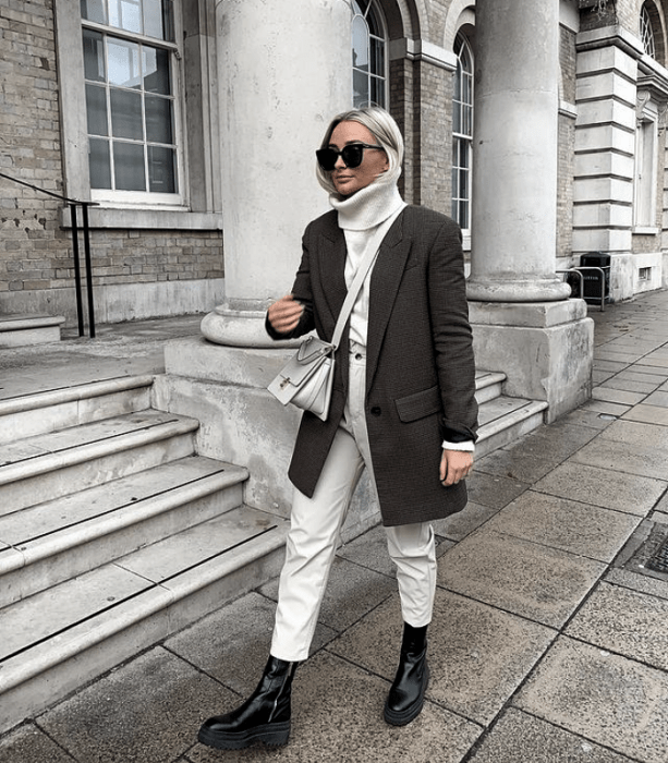 chica rubia platinada usando lentes de sol, suéter blanco de cuello alto, pantalones de mezclilla blanco, botas de cuero negras, 